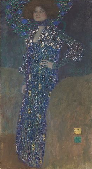 Stehende Frau in langem blau-goldenem gemusterten Kleid mit auffälligem, rundem Halskragen vor dunklem Hintergrund